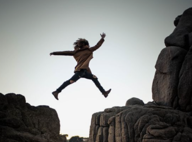 This image captures a person in mid-air, leaping between two large rocky cliffs, symbolizing boldness and the willingness to take risks. With arms stretched out and legs extended, the individual displays confidence and determination, embodying key qualities of resilience. The rugged, natural environment highlights the challenge being faced, while the leap suggests overcoming obstacles and embracing change. This visual resonates with the theme "Resilient People: 10 Traits of Highly Resilient People," emphasizing traits such as courage, adaptability, and perseverance in the face of adversity. The scene perfectly illustrates the essence of resilient individuals taking leaps toward growth and success.