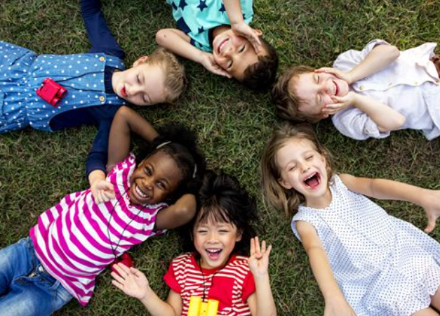 A group of diverse, happy children lying in a circle on the grass, smiling and laughing together, embodying the concept of "Unlocking the Emotional Strengths of a Child."